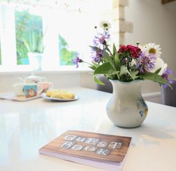 A kitchen countertop with a guest book a vase of flowers and a tray with cups and scones at Washpool in Milton-Under-Wychwood