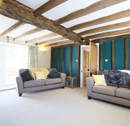 A living room with two sofas pillows exposed wooden beams and a wooden door at Washpool in Milton-Under-Wychwood