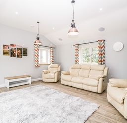 A living room with cream sofas a fluffy rug two windows with chevron curtains and a wall clock at Strawberry Stables in Iwood near Congresbury