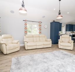 A living room with cream sofas, patterned curtains, a gray shag rug, and blue kitchen cabinets at Strawberry Stables in Iwood near Congresbury