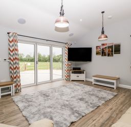 A living room with sliding glass doors a television on a stand a large rug and chevron patterned curtains at Strawberry Stables in Iwood near Congresbury