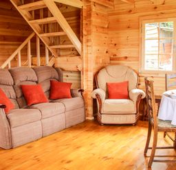 A wooden living area with a sofa and armchair with orange cushions and a dining table with chairs at Callow Fold in Dinchope near Craven Arms