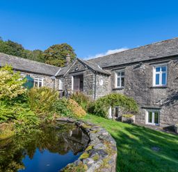 A stone house with white framed windows next to a garden pond and greenery at Field Head House in Graythwaite near Hawkshead