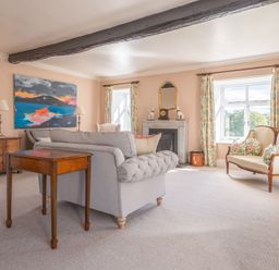 A sitting room with a grey sofa, wooden tables, a fireplace, floral curtains, and a cream settee at Field Head House in Graythwaite near Hawkshead