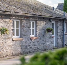 A stone exterior wall with white windows and hanging flower baskets at Grubbings Graythwaite near Hawkshead