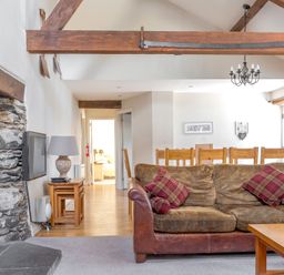 A living room with a brown sofa and red cushions a stone fireplace wooden dining table and chairs at Grubbings Graythwaite near Hawkshead