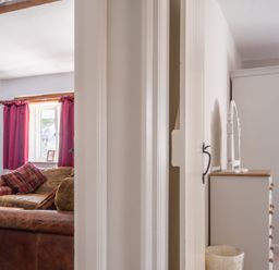 A living room with brown sofas and red curtains next to a bedroom with white furniture at Grubbings Graythwaite near Hawkshead
