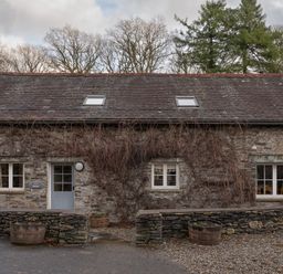 Stone cottage with a gray door and windows with vines on the facade and barrel planters at Bull Pen in Graythwaite near Hawkshead
