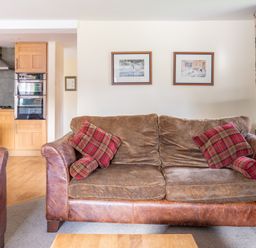 A living room with a brown sofa and red plaid cushions next to a kitchen with wooden cabinets at Bull Pen Graythwaite near Hawkshead