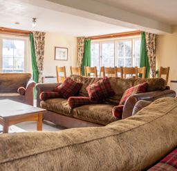 A living room with brown sofas and plaid cushions near a wooden dining table with chairs at Bull Pen in Graythwaite near Hawkshead