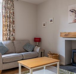 A living room with a gray sofa and blue patterned cushions a wooden coffee table a fireplace with a wood stove and a painting of a hare above it at Briar in Graythwaite near Hawkshead