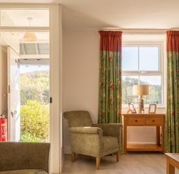 A sitting area with armchairs and a wooden table under a window with floral curtains at Eel House Cottage Graythwaite Estate near Hawkshead