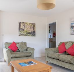 A living room with two green sofas with red and green cushions a wooden coffee table and paintings on the walls at Eel House Cottage in Graythwaite Estate near Hawkshead