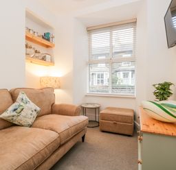 A living room with a brown sofa a small table an ottoman a wall-mounted television and a cabinet with a plant and decorative bowl at Pottergill in Windermere