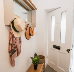 An entryway with a white front door a coat rack with hats and a scarf a small wooden bench with a potted plant and a woven basket next to the door at Pottergill in Windermere