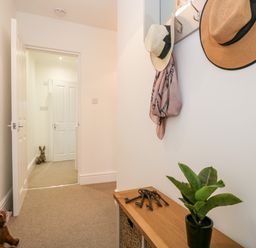 A hallway with a wooden bench holding a plant and keys two hats and a scarf hanging on hooks and an open door showing another hallway with a rabbit figurine at Pottergill in Windermere