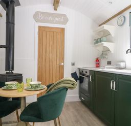 A kitchen and dining area with green chairs wooden table green cabinets and a wood stove at High Rigg Shepherd's Hideaway in Brampton Cumbria
