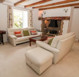 A living room with white sofas a wooden coffee table a stone fireplace and exposed wooden ceiling beams at 1A Chantry Place in Morpeth