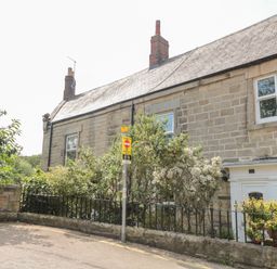 A stone house with two chimneys and a small front garden behind a black metal fence at 1A Chantry Place in Morpeth