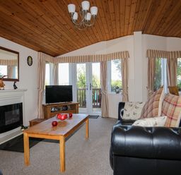 A living room with a wooden coffee table black sofa and a fireplace at Ffrwd Lodge in Rhosneigr