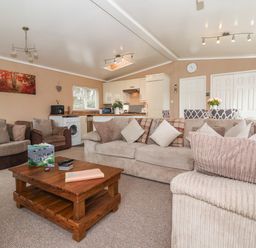 A living room with beige sofas and a wooden coffee table with a kitchen and dining area in the background at Jonstone Pines in Cayton Bay near Scarborough