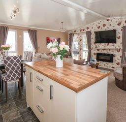 An open living and dining area with a kitchen island a dining table and chairs a sofa and a wall-mounted television at Jonstone Pines in Cayton Bay near Scarborough