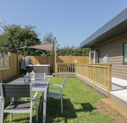 An outdoor area with a table and four chairs on grass a wooden fence a hot tub with a canopy and a wooden deck attached to a building at Bluebell Wood in Brandesburton