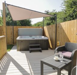 An outdoor patio area with a hot tub under a sunshade and a wicker table and chair set with glasses at Bluebell Wood in Brandesburton