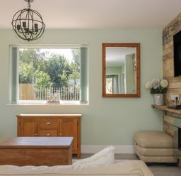 A living room with a wooden coffee table a window with vertical blinds a wall clock a mirror a wooden sideboard a wall-mounted television a flower pot and a fireplace at Bluebell Wood in Brandesburton