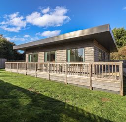 A wooden building with a deck and grass area at Bluebell Wood in Brandesburton