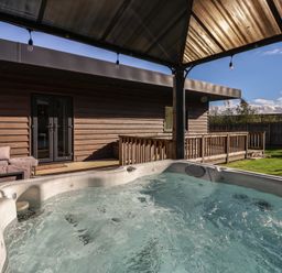 A hot tub near a wooden deck and couch at Bluebell Wood in Brandesburton