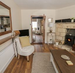 A living room with a fireplace chair coffee table and mirror at Thimble Cottage in Winchcombe