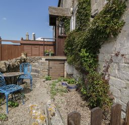 A small outdoor patio with two blue metal chairs a round table a stone wall and climbing plants on a cottage wall at Athelstan Cottage Chloe Mead near Stroud