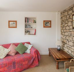 A sitting area with a red covered sofa with cushions a wooden coffee table with a lamp a wicker basket and a stone wall with a mirror at Athelstan Cottage in Chloe Mead near Stroud