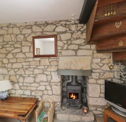 A room with a stone fireplace and wood burning stove a wooden table with a lamp and a television at Athelstan Cottage Chloe Mead near Stroud