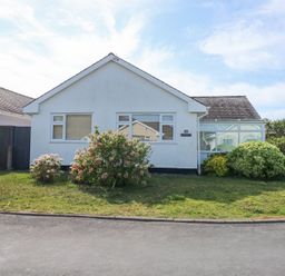 A single story white house with shrubs and a lawn at Glanaig in Morfa Bychan