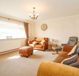 A living room with brown leather sofas a green armchair a wooden side table and a large window at Glanaig in Morfa Bychan