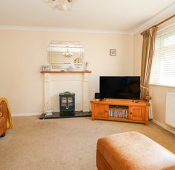A living room with a television on a wooden stand a fireplace a brown sofa and a window with curtains at Glanaig in Morfa Bychan