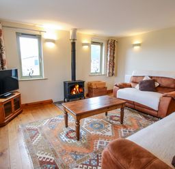 A living room with two sofas a wooden coffee table a patterned rug a wood burning stove and a television at Norton Cottage in Craven Arms