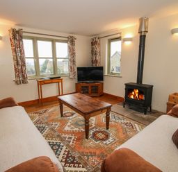 A living room with two sofas coffee table wood stove and television at Norton Cottage in Craven Arms