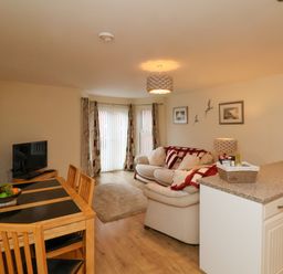 An open living room and dining area with a wooden dining table and chairs a sofa with cushions and a coffee table at Cadliam in Whitby