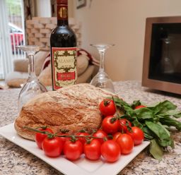 A kitchen counter with a loaf of bread cherry tomatoes basil bottle of red wine and two upside down wine glasses at Cadliam in Whitby