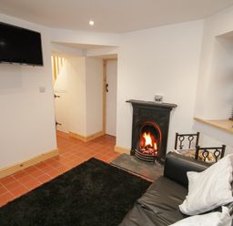 A living room with a black sofa white pillows a fireplace wall mounted television and a window with blinds at Old Tollgate in Gwalchmai near Llangefni
