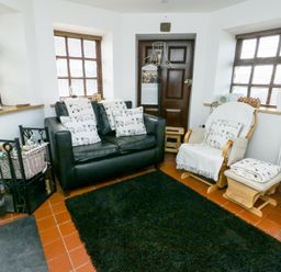 A sitting room with a black leather sofa and a wooden rocking chair with cushions at Old Tollgate in Gwalchmai near Llangefni