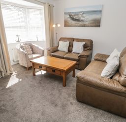 A living room with two brown leather sofas a wooden coffee table an upholstered armchair and a window with blinds and curtains at Seadrift The Bay near Filey