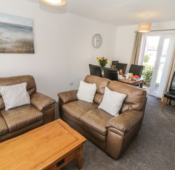 A living room with brown leather sofas and a wooden coffee table and a dining table set with black chairs and flowers at Seadrift The Bay near Filey