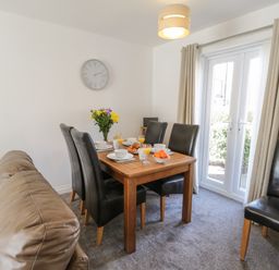 A dining area with a wooden table set for breakfast with black chairs and beige curtains at Seadrift The Bay near Filey