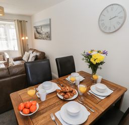 A dining table set with plates bowls croissants and orange juice next to a living room with sofas and a chair at Seadrift The Bay near Filey