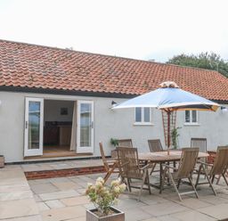 An outdoor patio area with a wooden table and chairs under a blue umbrella at Waveney View Cottage in Burgh Castle
