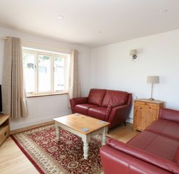 A living room with red leather sofas a wooden coffee table a television on a wooden stand and a patterned rug at Waveney View Cottage in Burgh Castle